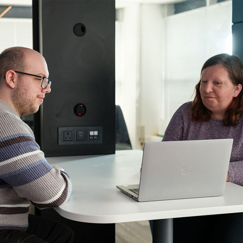 Two people smiling and using laptops