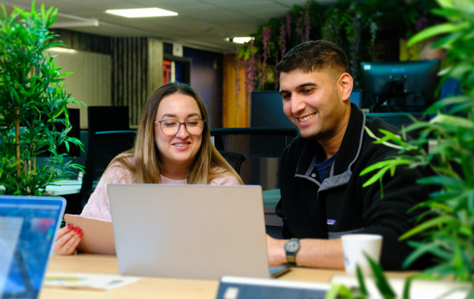 two work colleagues look at a laptop screen together in a creative, quirky office space