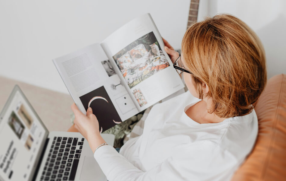 a woman peruses a sleek lifestyle brochure whilst balancing her laptop on her knee