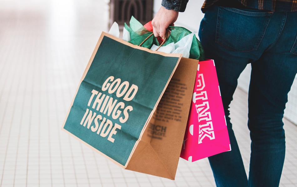 a person struggles to carry multiple shopping bags whilst one of the bags says 'good things inside'