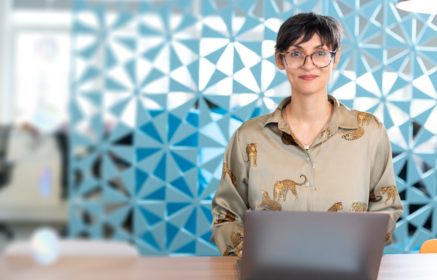 A friendly technician smiles at the camera whilst sitting at her desk with a laptop