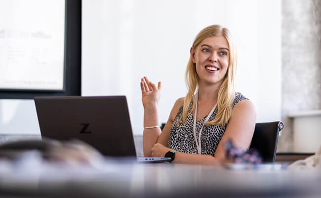 A young PCC specialist smiles at a camera whilst sitting in front of a computer monitor