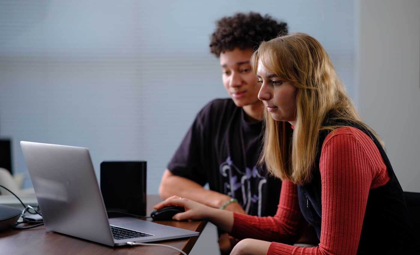 Two people gather around a laptop in a boardroom looking at PPC campaign statistics