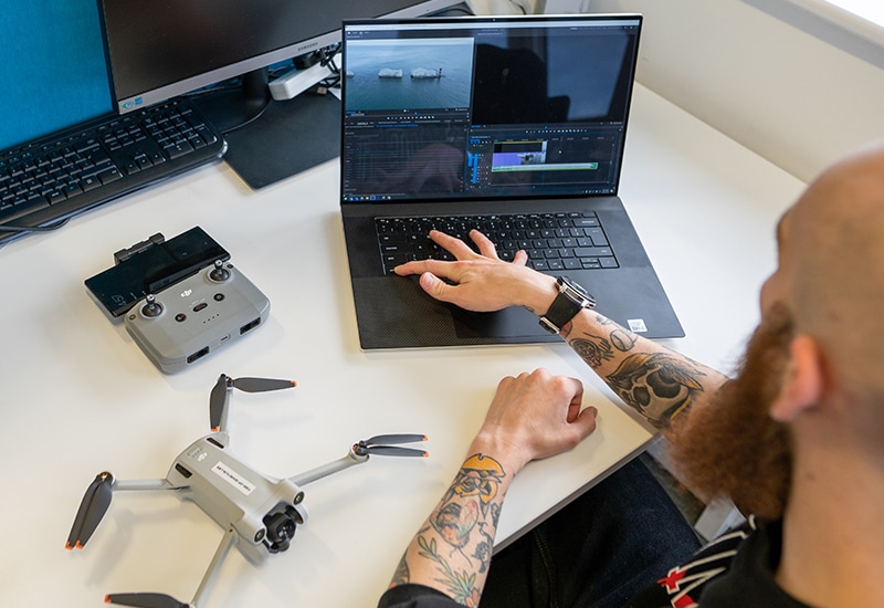 A post-production videographer edits some drone footage on their laptop